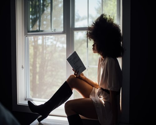 Person reading a book near a large bright window